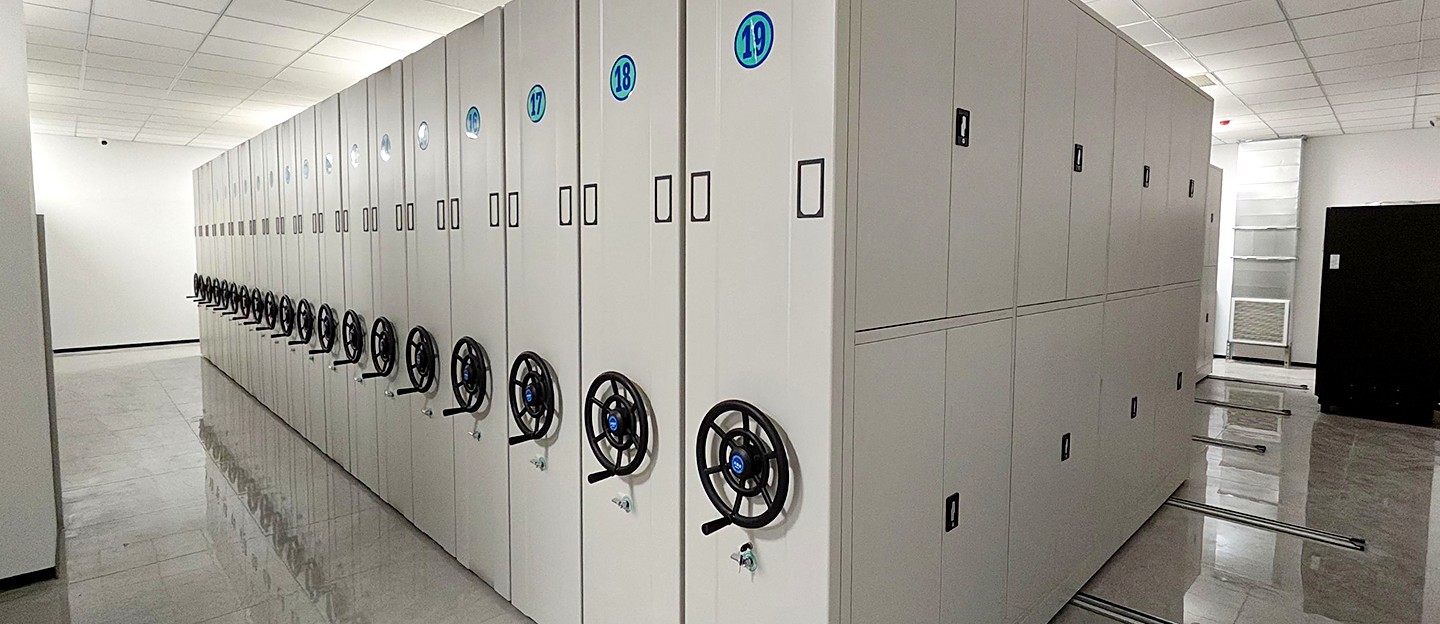Nineteen-bay manual compactor run with round number badges in an archive storeroom