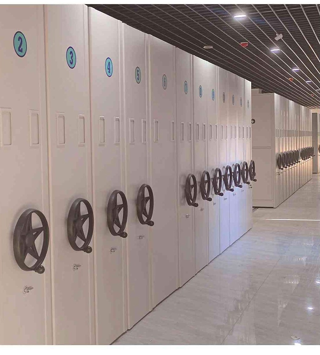 Long manual compactor run with numbered bays and five-spoke wheels in a records hall
